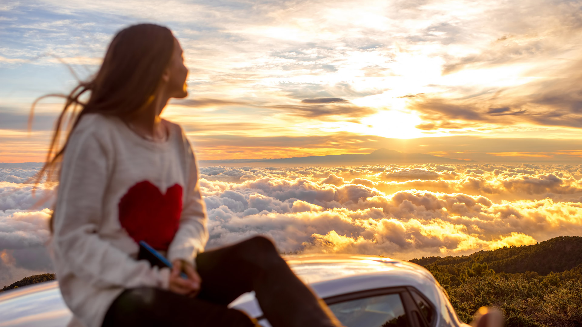 A young woman looking out over a scenic vista after driving her car up a mountain