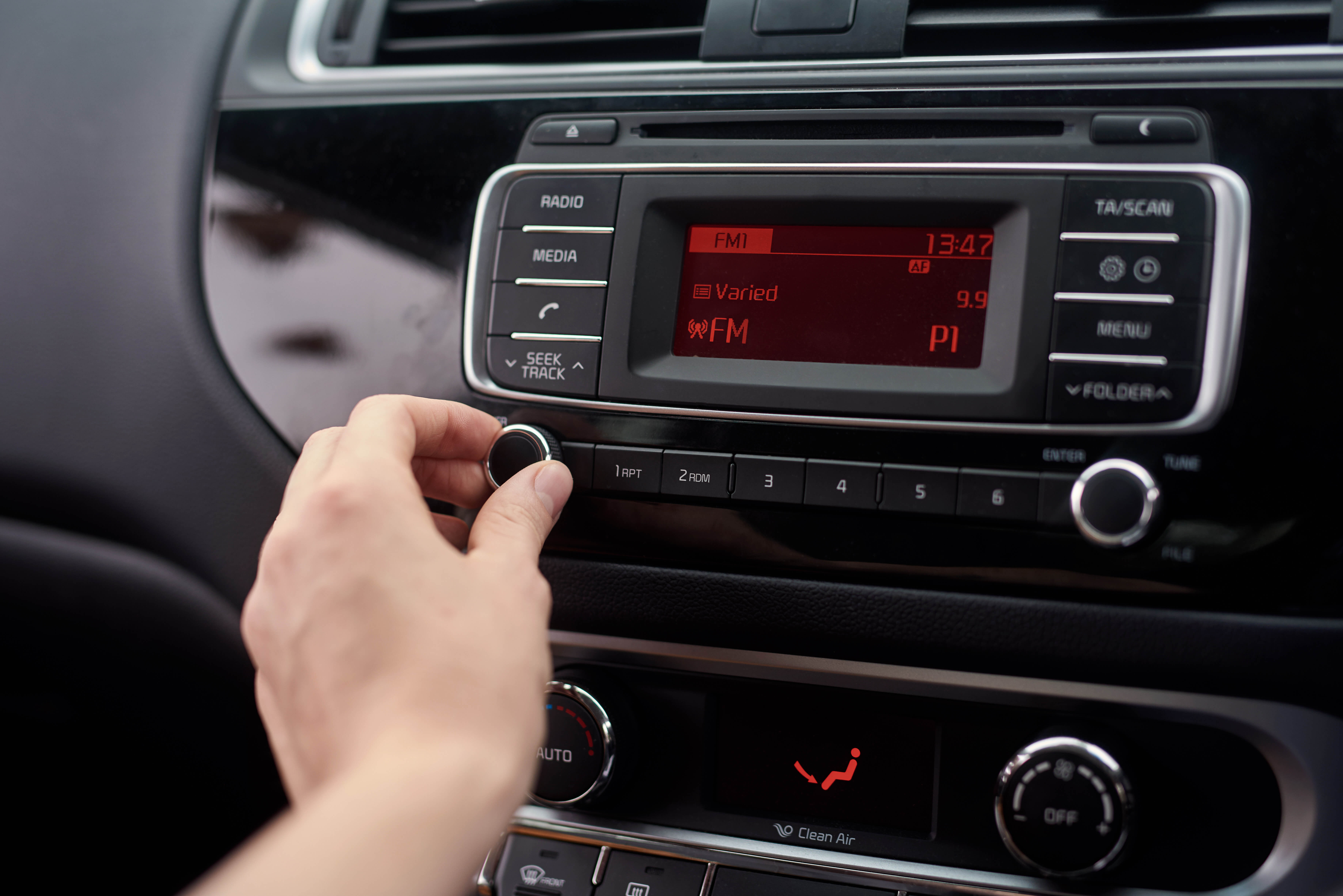 person adjusting the volume on their car radio