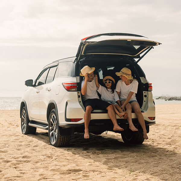 Family sitting in boot of car at beach